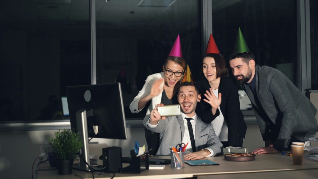 Colleagues celebrating with party hats taking a selfie.