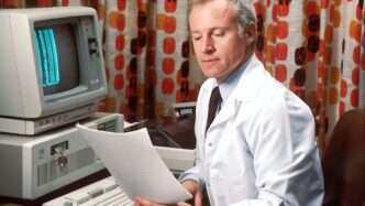 man reading papers in front of computer