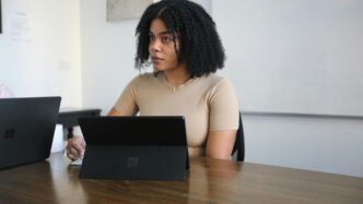 Female worker sitting in a board room with black Surface laptop on the table