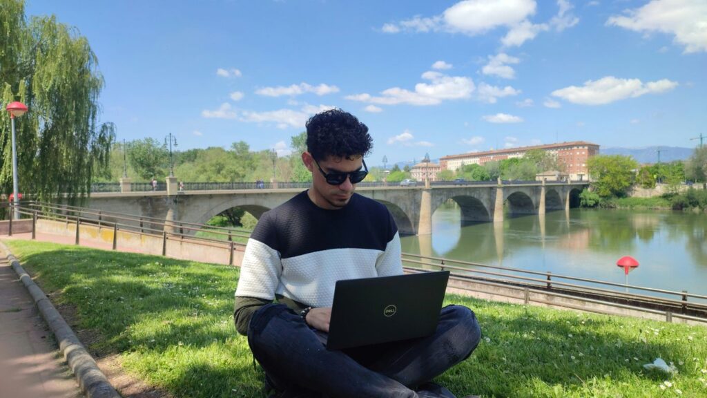 a man sitting on grass with a laptop
