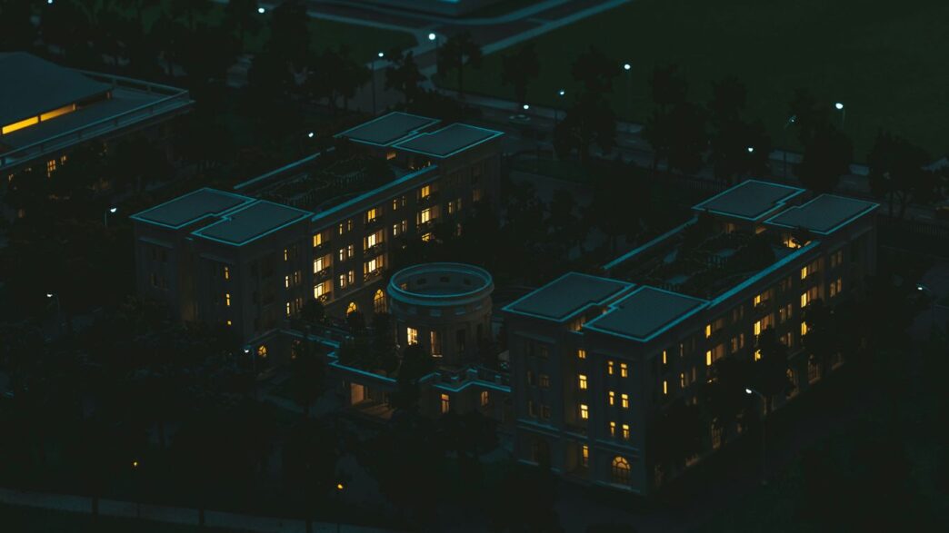 Illuminated building complex at night with surrounding green space.