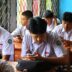 Students in uniform using phones in classroom.