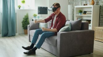 Man wearing vr headset plays video game on couch.