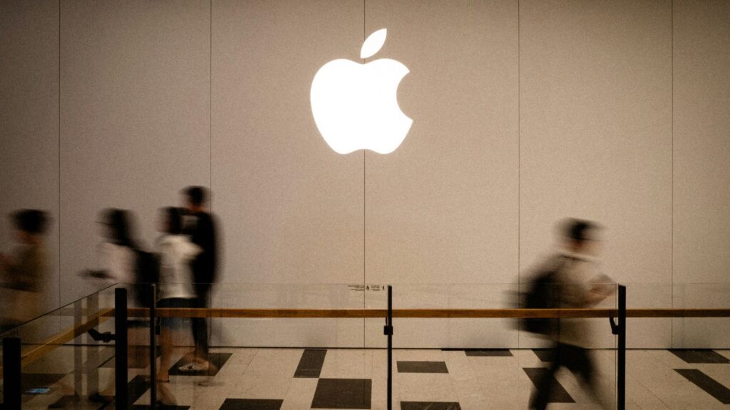 People walk past a large glowing apple logo.