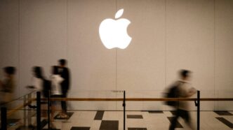 People walk past a large glowing apple logo.