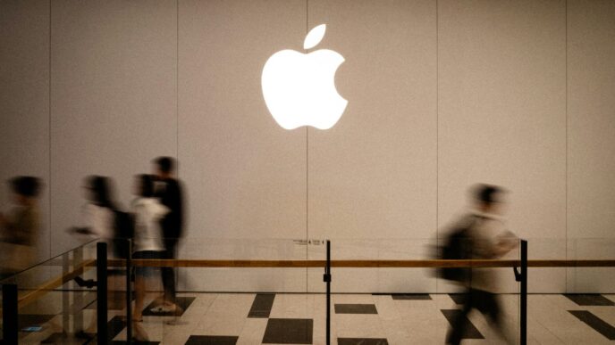 People walk past a large glowing apple logo.