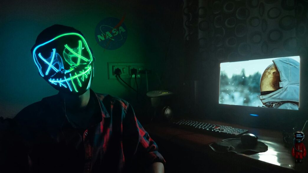 person in blue and green LEd mask sitting in front of turned-on computer monitor