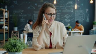 Woman talking on phone at desk with laptop
