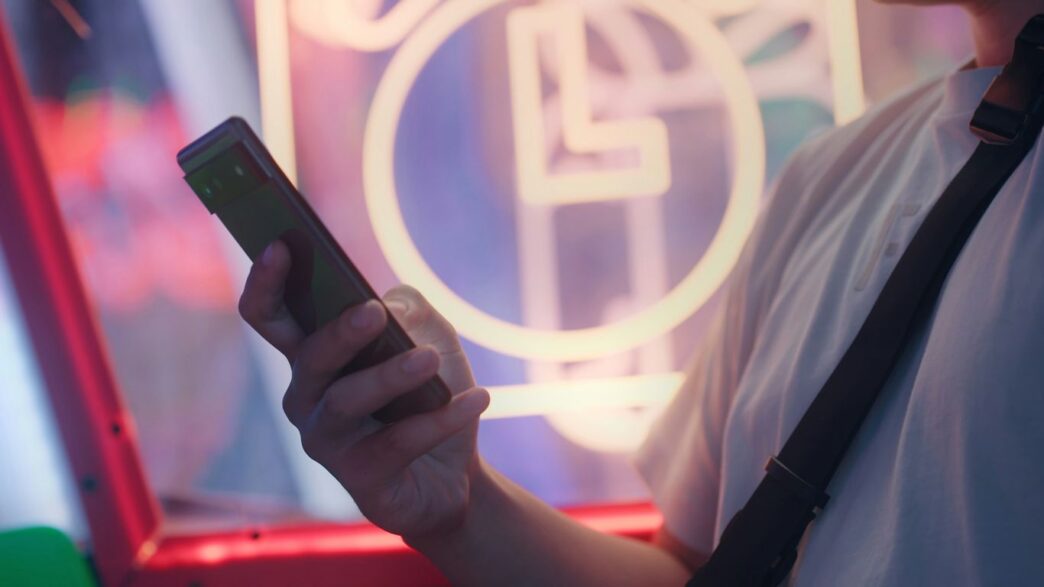 a man holding a cell phone in front of a neon sign