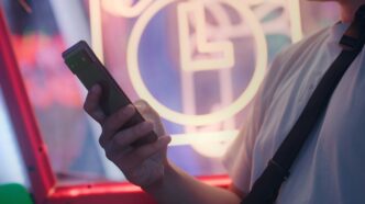a man holding a cell phone in front of a neon sign
