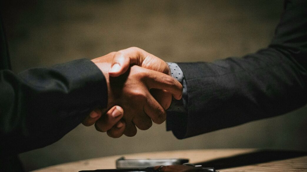 two people shaking hands over a wooden table