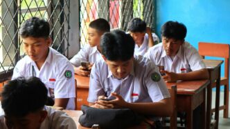 Students in uniform using phones in classroom.