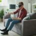 Man wearing vr headset plays video game on couch.