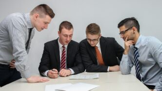 four men looking to the paper on table