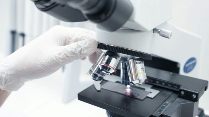 A person in white gloves looking through a microscope