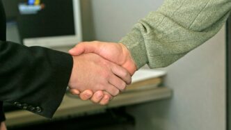 two people shaking hands in front of a computer monitor