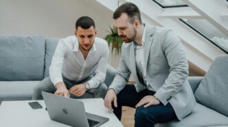 two men looking at a laptop on a table