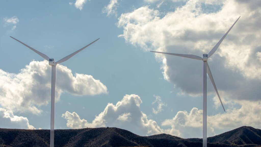 Two wind turbines on a hill under clouds.