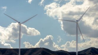 Two wind turbines on a hill under clouds.