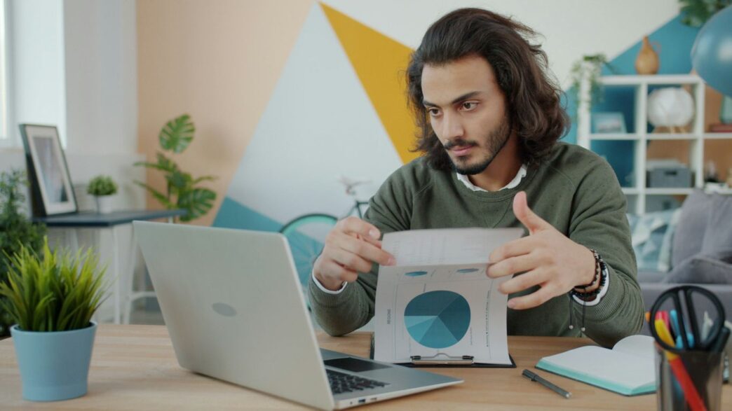 Man looking at laptop and paper in colorful room