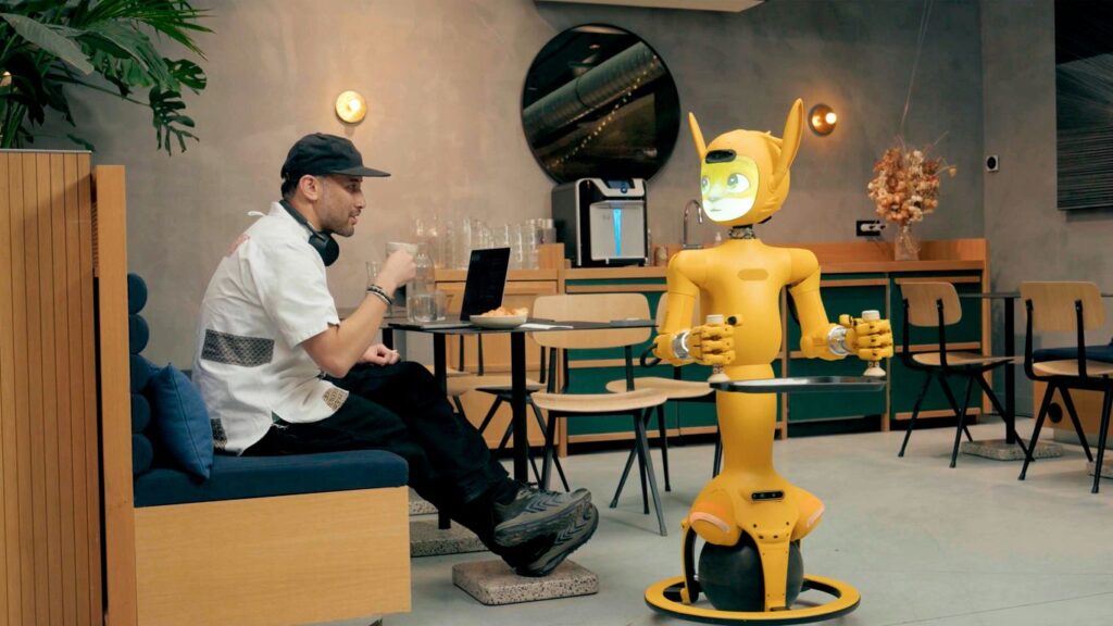 Man in cafe interacts with a yellow robot.