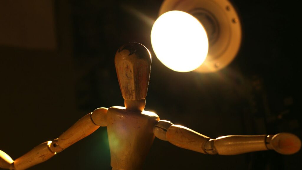 a wooden mannequin standing in front of a light