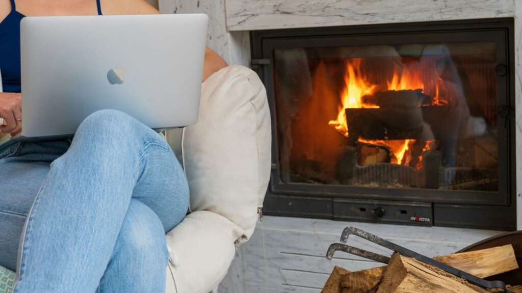 a woman sitting in a chair with a laptop in front of a fireplace
