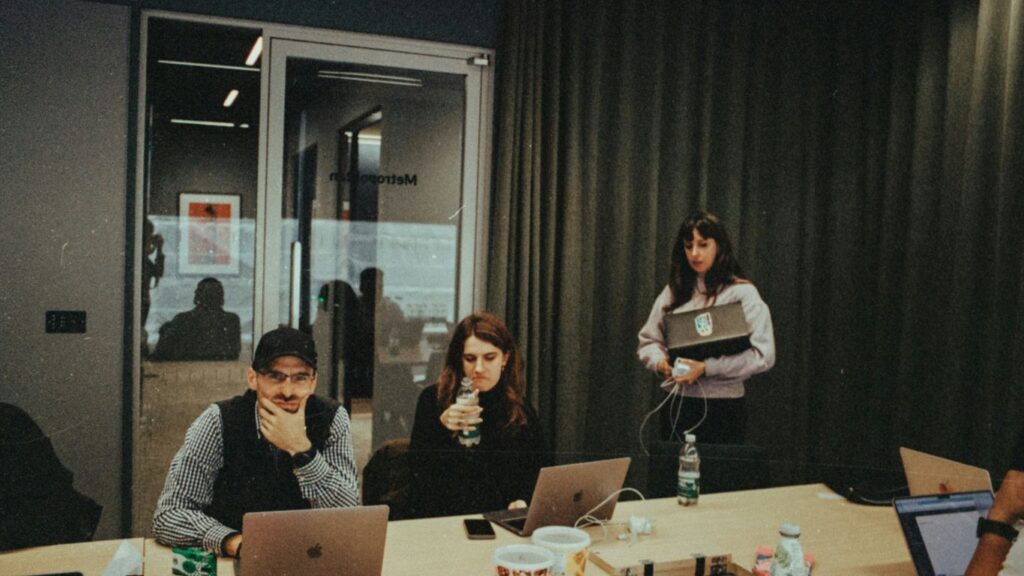 a group of people sitting around a table with laptops