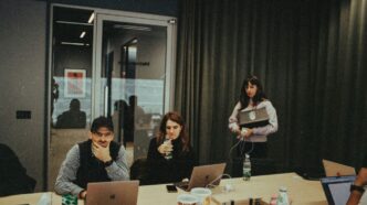 a group of people sitting around a table with laptops
