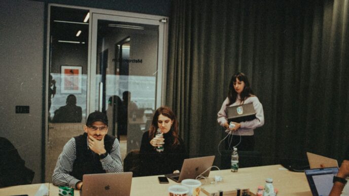 a group of people sitting around a table with laptops