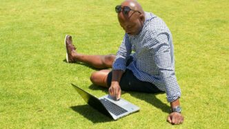 man in blue and white checkered button up shirt sitting on green grass field