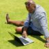 man in blue and white checkered button up shirt sitting on green grass field