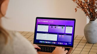 Woman using laptop with october 2025 calendar displayed.