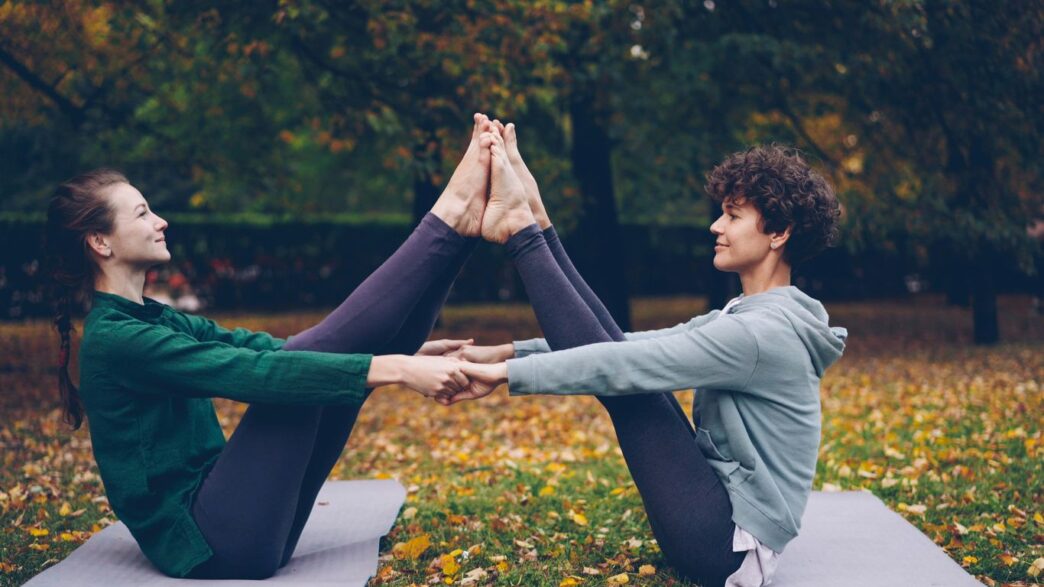 Two women doing partner yoga in a park.