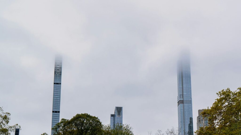 Skyscrapers emerge from a thick, foggy sky.