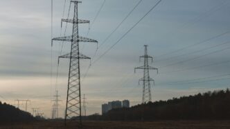 Power lines stretch across a field towards distant buildings.