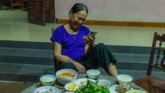 a woman sitting at a table full of food looking at her cell phone
