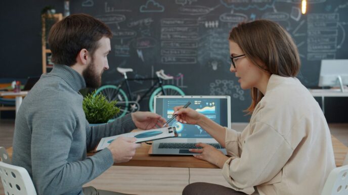 Two colleagues reviewing data on a laptop.