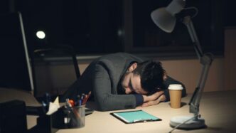 Man sleeping at desk with coffee and tablet.