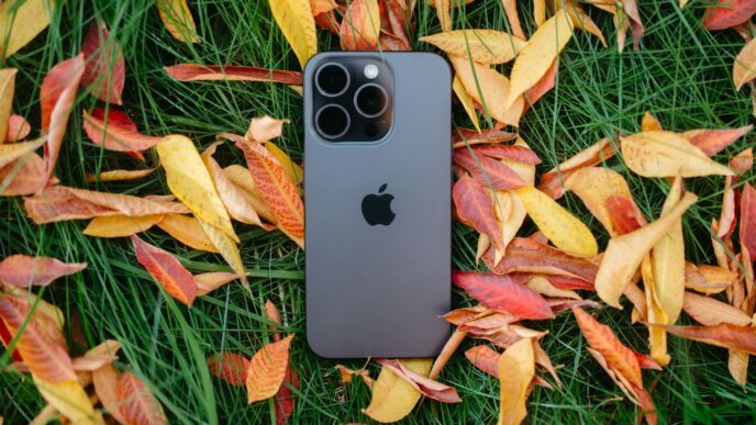 An iPhone is laying in the grass surrounded by autumn leaves
