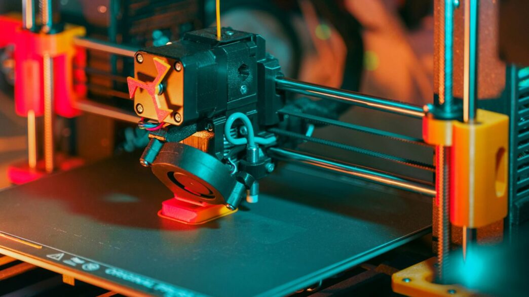 3D printer creating a red object with yellow filament.