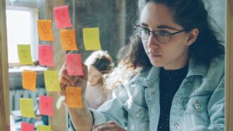 Woman analyzes colorful sticky notes on glass.