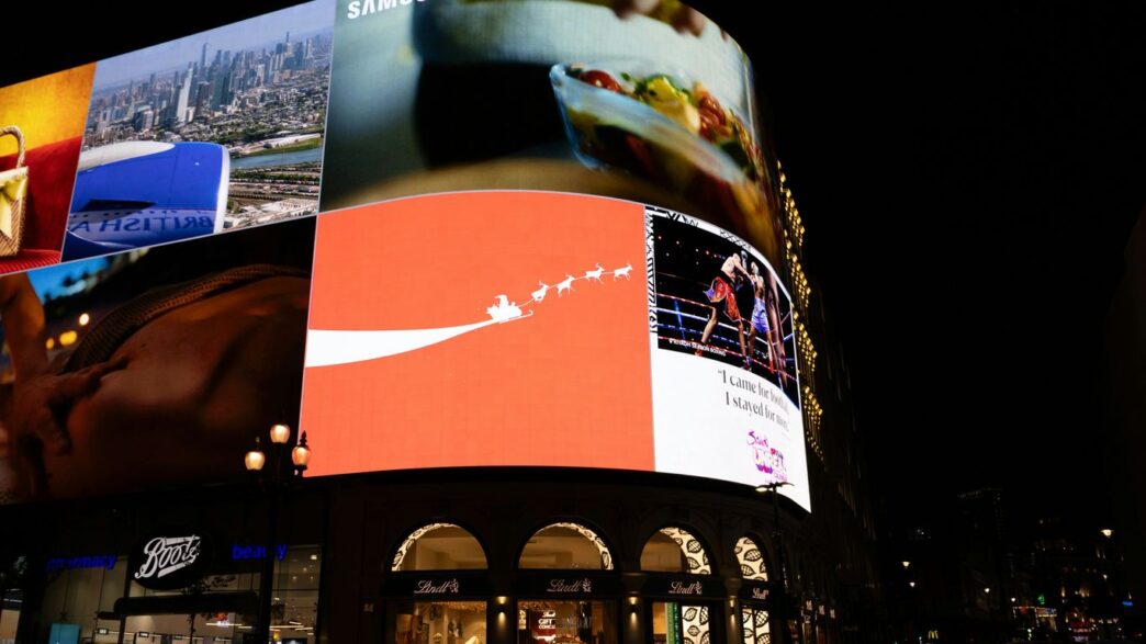 Bright digital billboards illuminate a city street at night.
