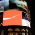 Bright digital billboards illuminate a city street at night.