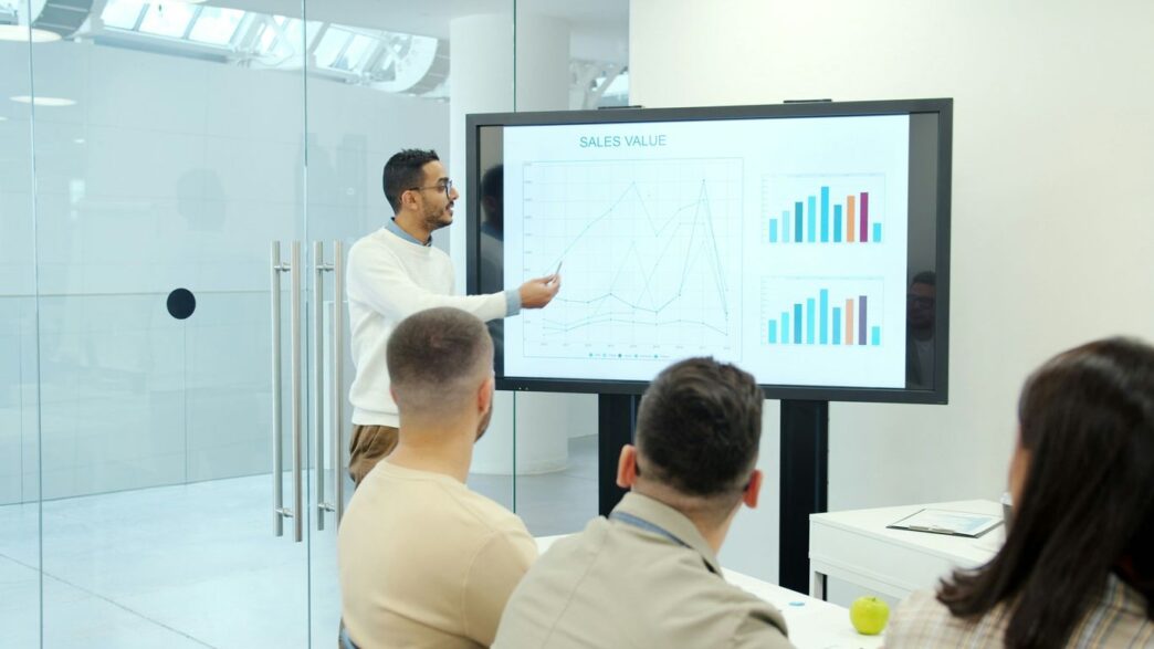 Man presenting charts on a large screen to audience.