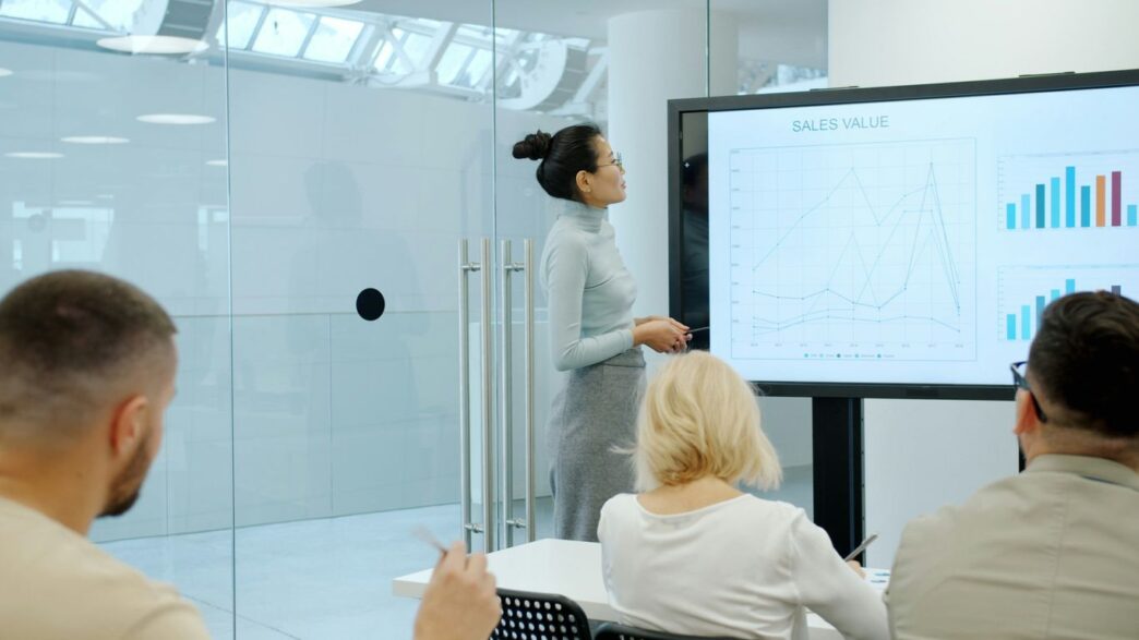 Woman presents charts on a screen to colleagues.