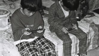 two young boys sitting on a bed looking at their cell phones