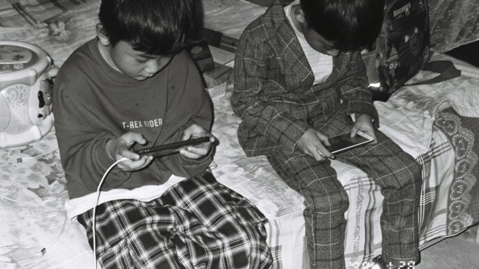 two young boys sitting on a bed looking at their cell phones