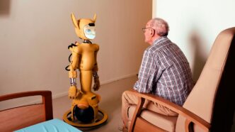Elderly man converses with a yellow robot.