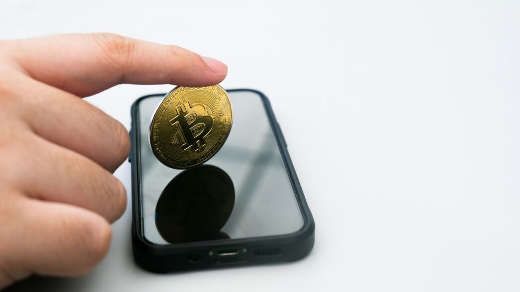 a person holding a gold coin in front of a cell phone